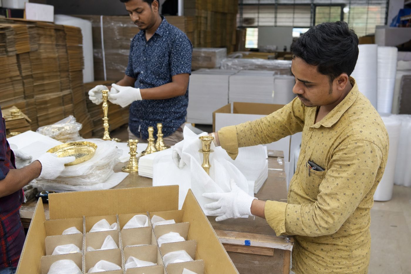Workers foam-wrapping polished Indian brass décor with anti-tarnish paper and carton dividers for export