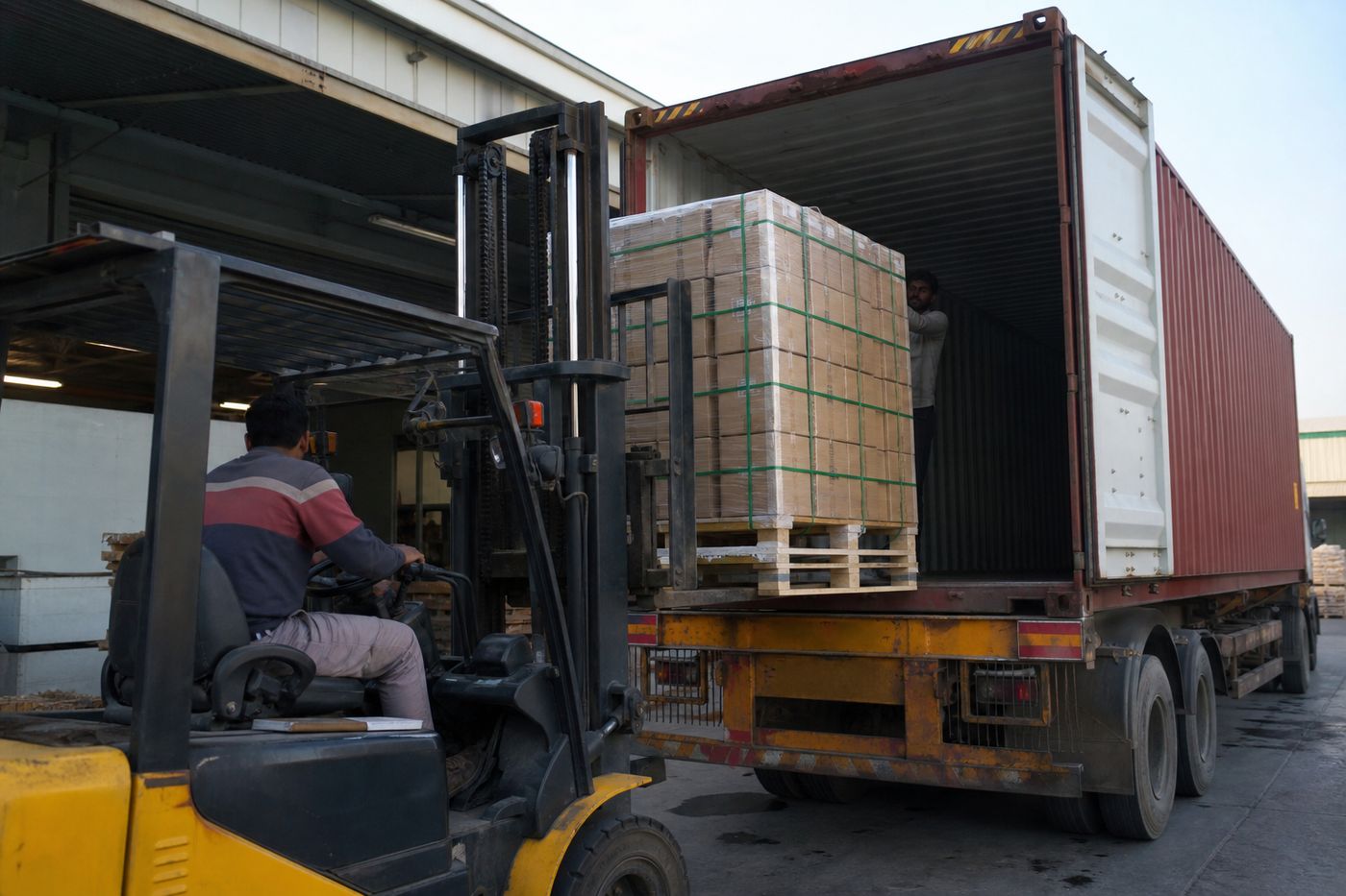 Forklift loading palletized Indian brass decorative cartons onto an export freight truck at a warehouse dock