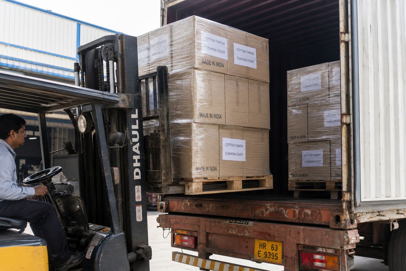Forklift loading shrink-wrapped pallets of cotton throw and cushion cover cartons into a freight truck at an Indian textile warehouse dock