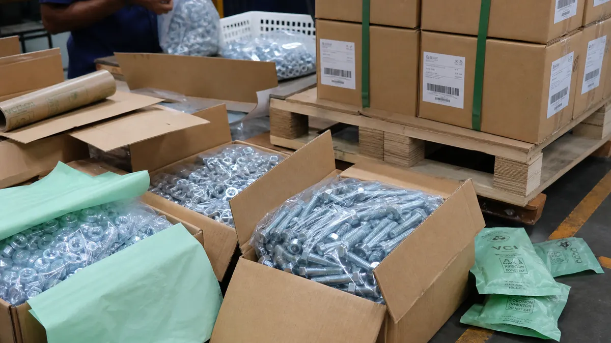 Workers packing poly-bagged bolts and nuts into corrugated export cartons on a pallet with VCI rust-protective materials