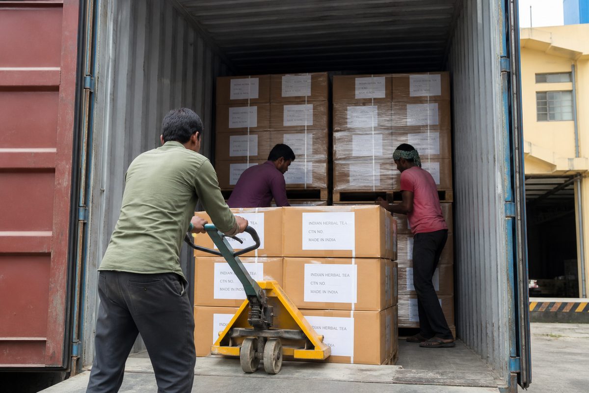 Workers stuffing palletized Indian herbal tea master cartons into a 20-foot export shipping container