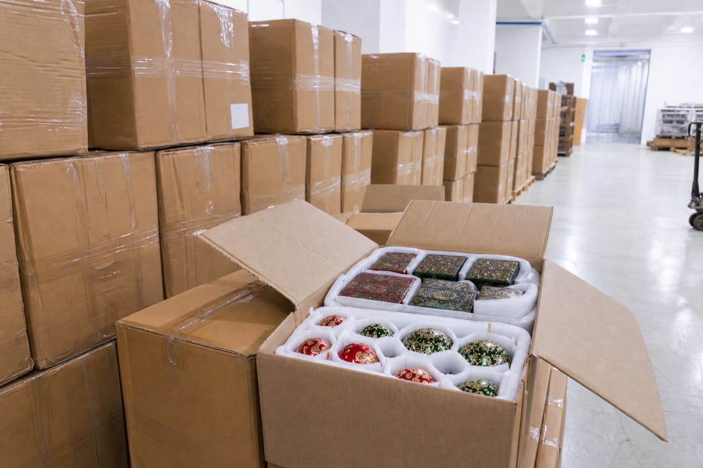 Palletized cartons of Indian papier-mache giftware in an export warehouse with open carton showing foam-wrapped lacquer boxes