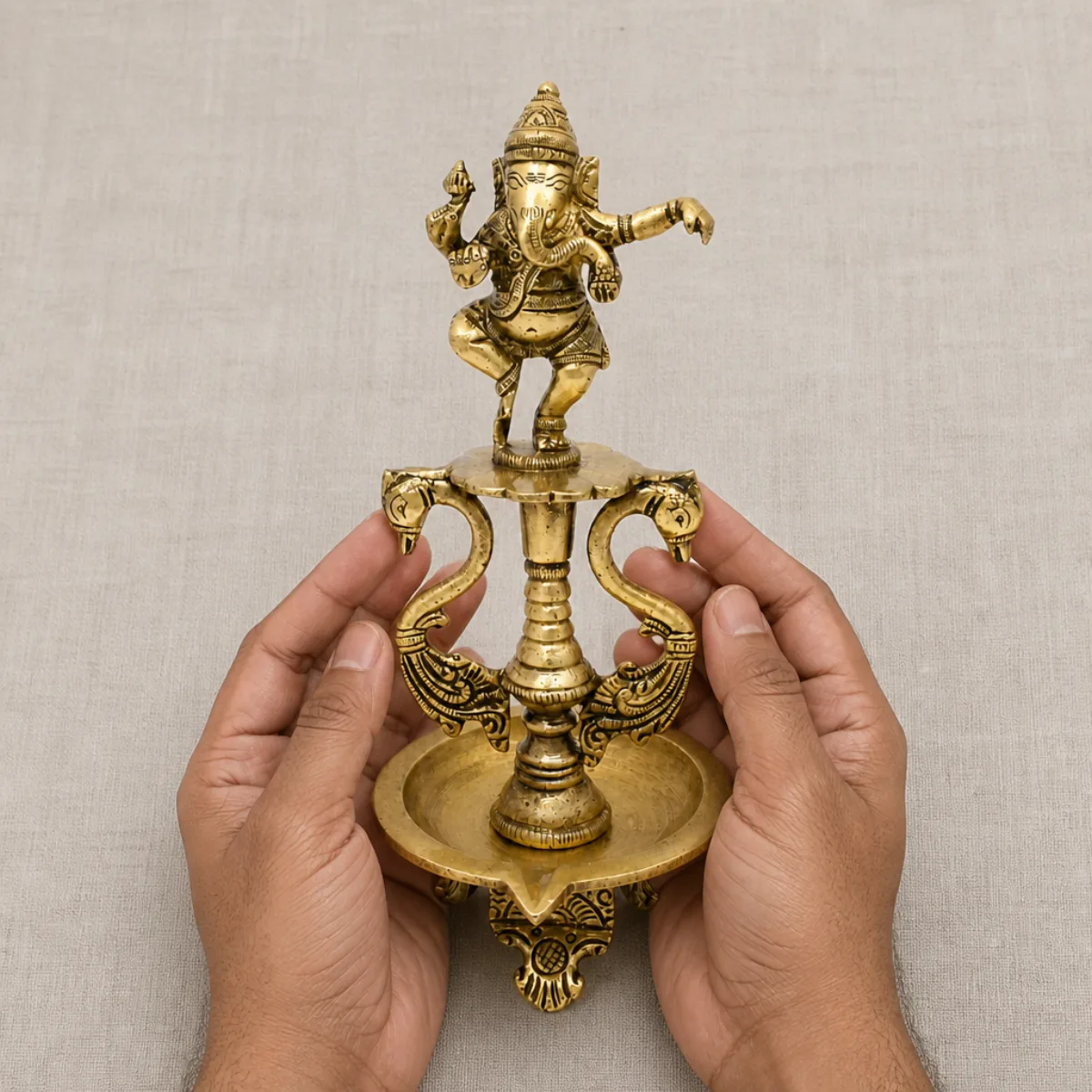 Hands holding an 8 inch handmade brass dancing Ganesha diya to show scale