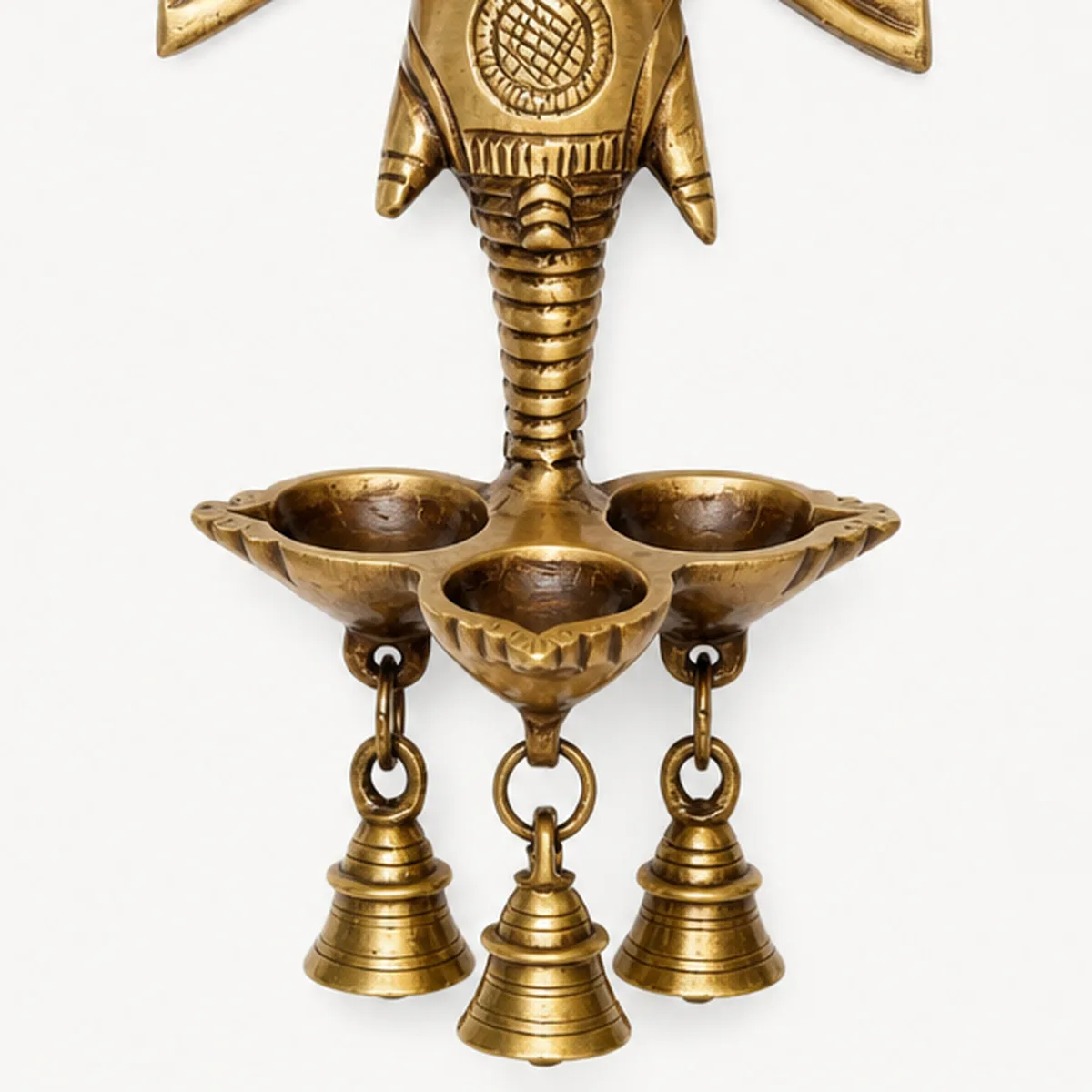 Close-up of three hanging brass bells under the deepak bowls of a Ganesha wall hanging