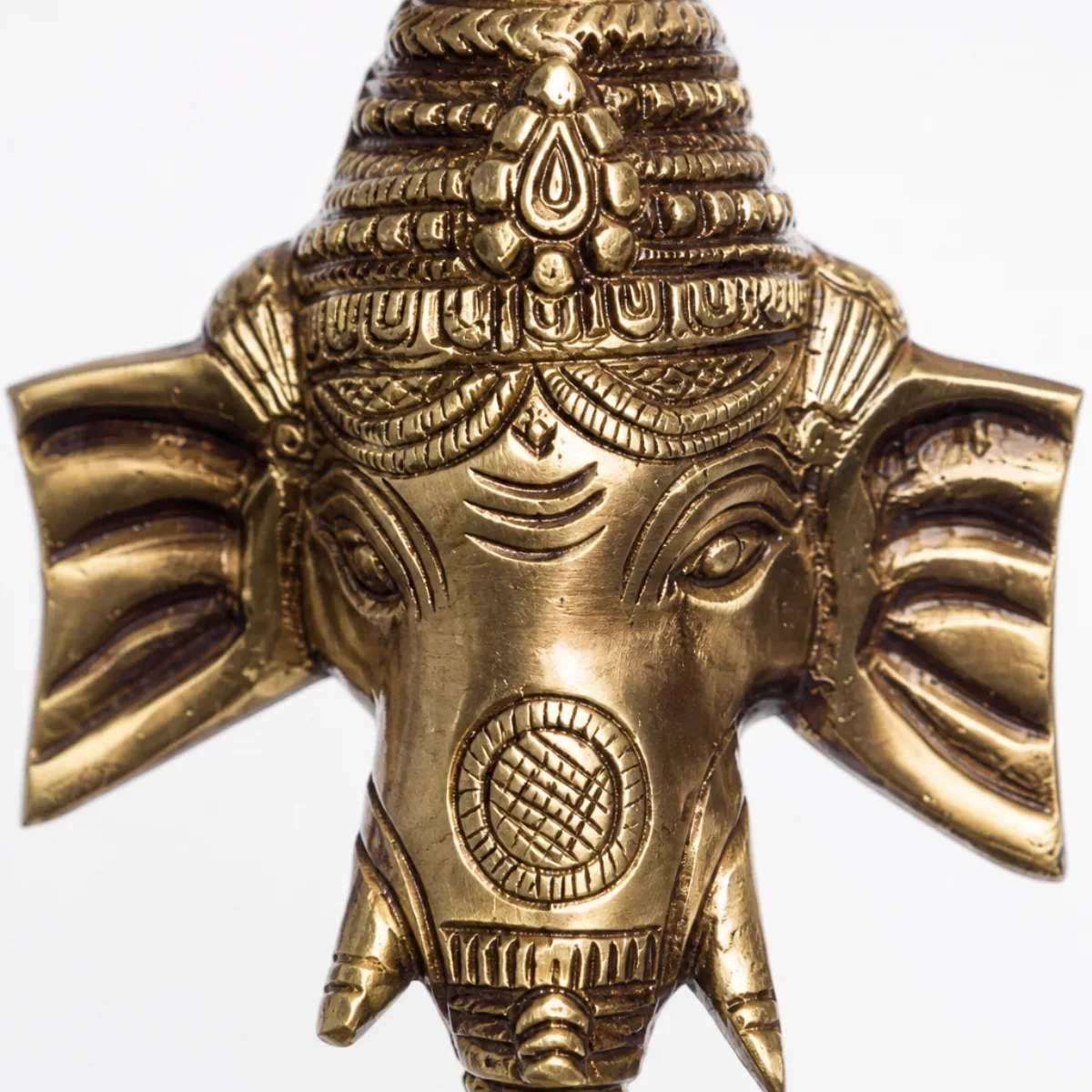 Close-up of the engraved brass Ganesha face and tall crown on a wall hanging