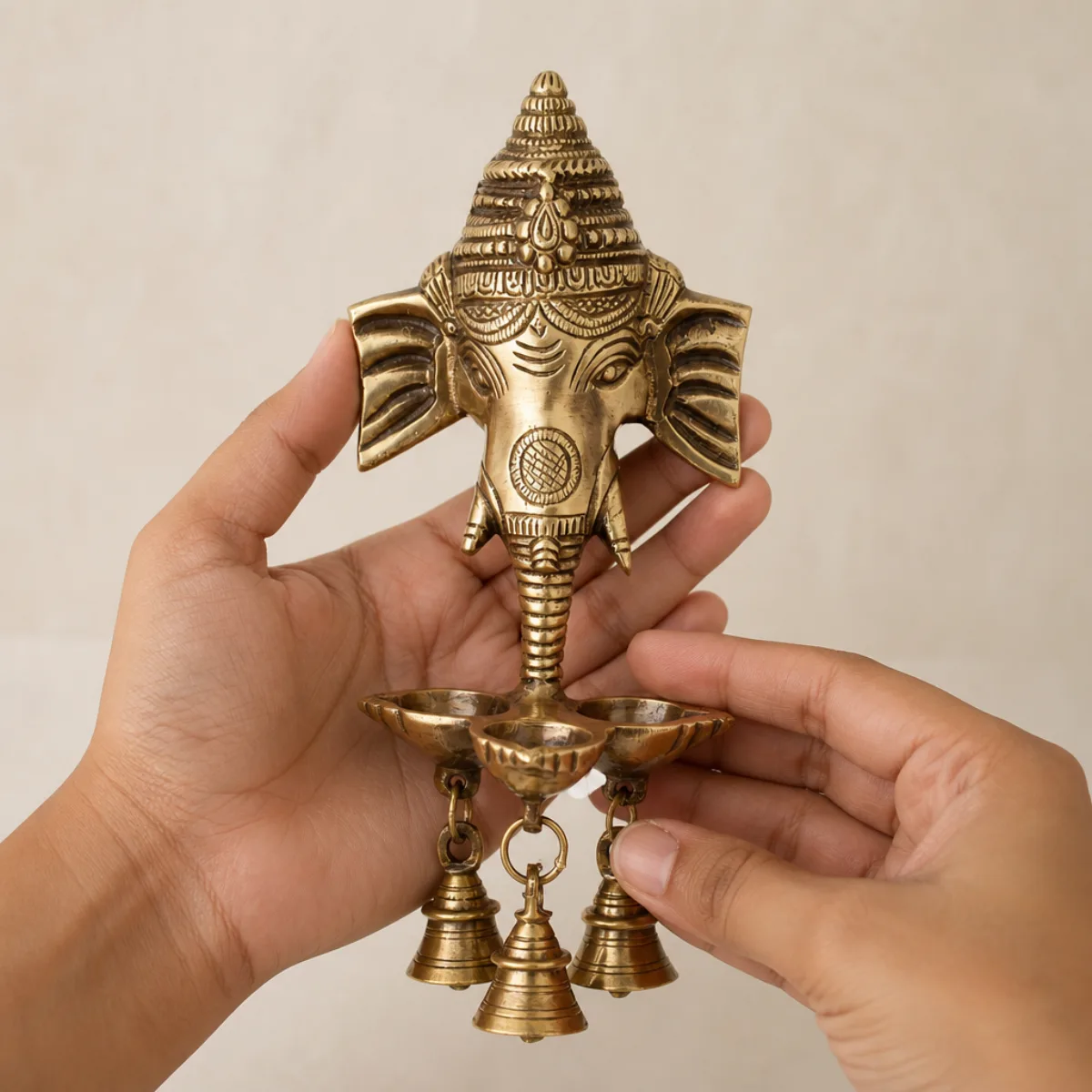 Hands holding a 24 cm handmade brass Ganesha deepak wall hanging to show scale
