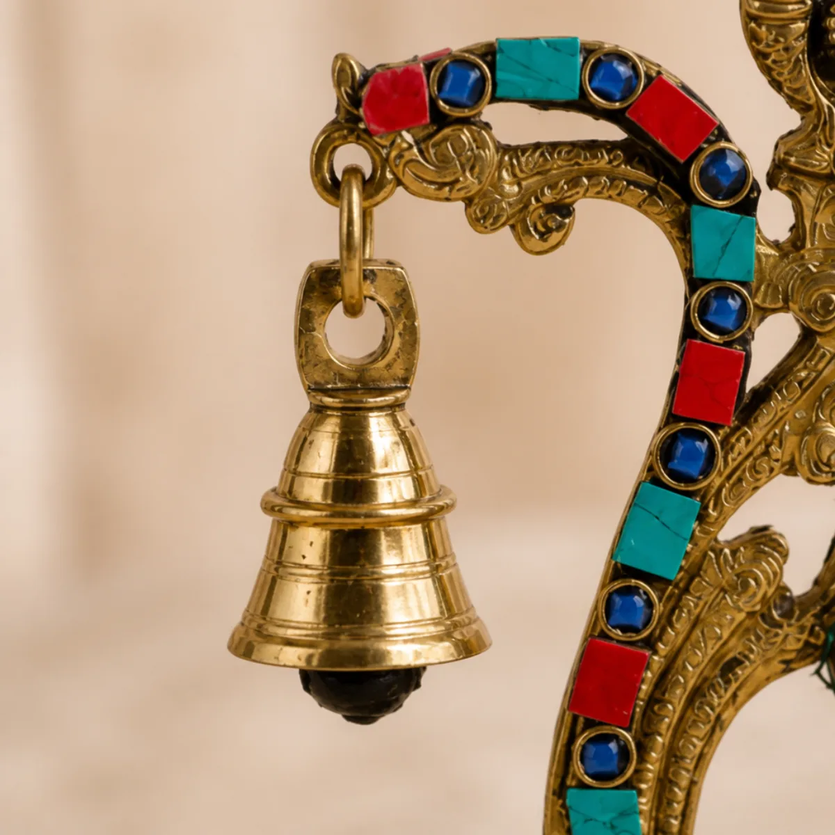 Close-up of the hanging brass bell on a gemstone peacock diya