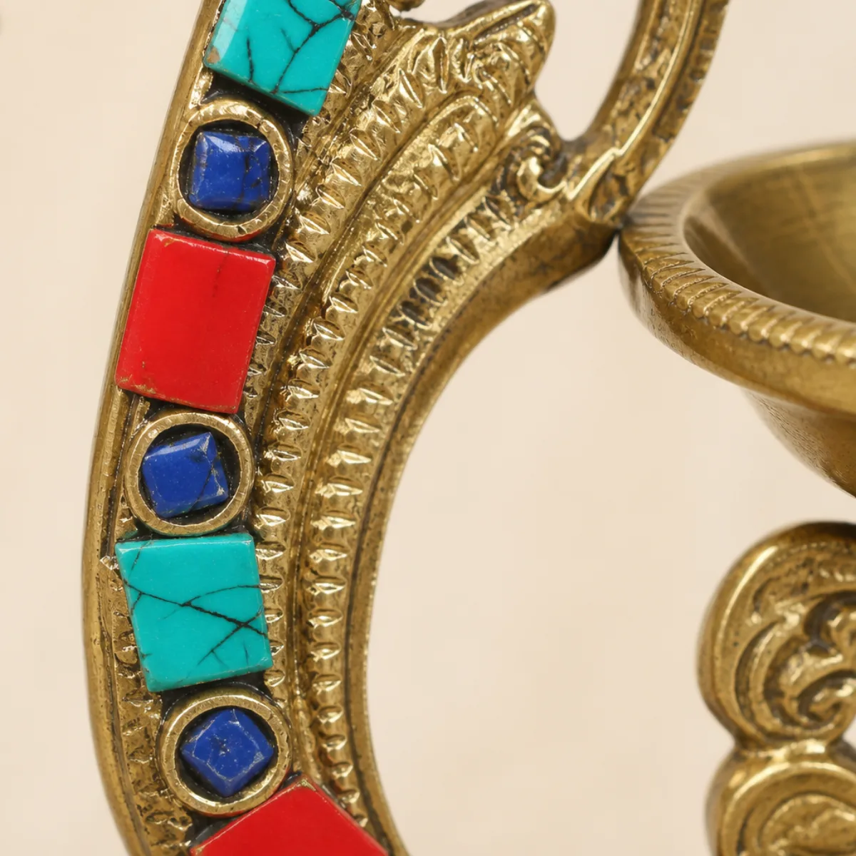 Close-up of turquoise, coral-red, and dark-blue stone mosaic on a brass peacock diya