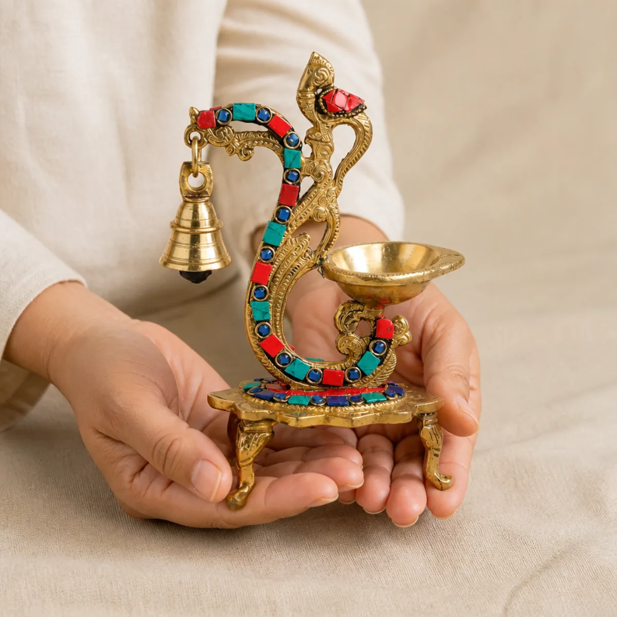 Hands holding an 8 inch handmade brass peacock gemstone diya to show scale