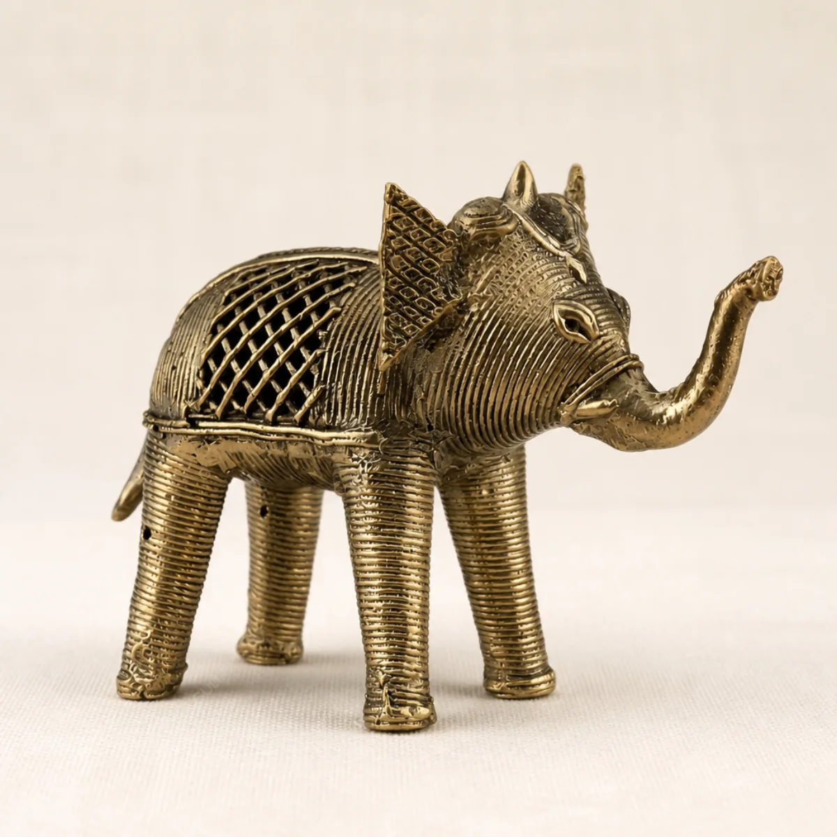 Side view of a handmade Dhokra brass elephant with lattice flank and raised trunk