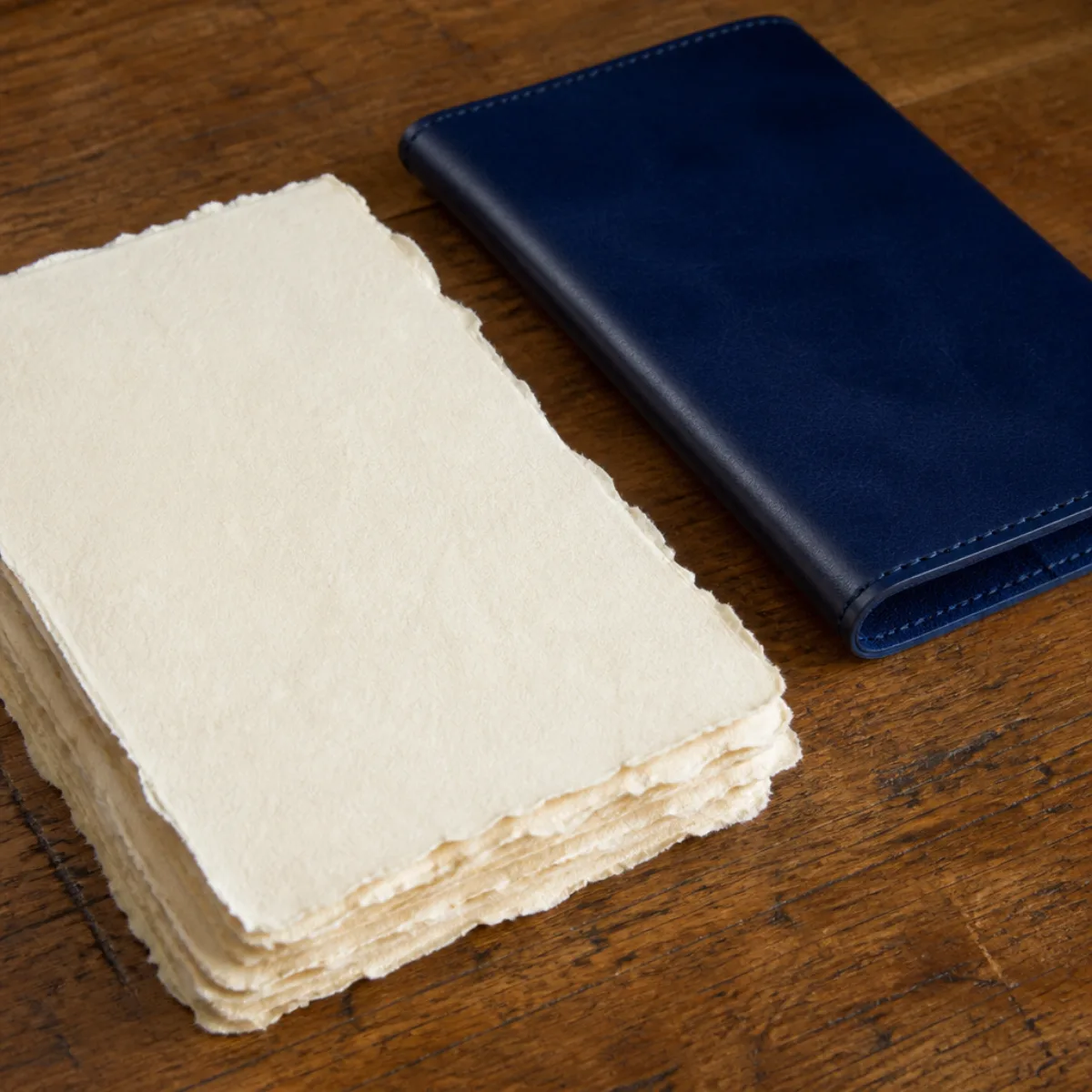 Handmade deckle-edge paper sheets and a navy-blue leather cover on a workshop table