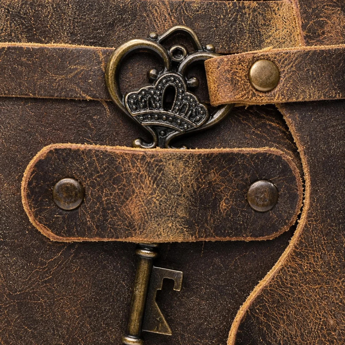 Close-up of antique bronze heart-and-crown key on a leather journal strap