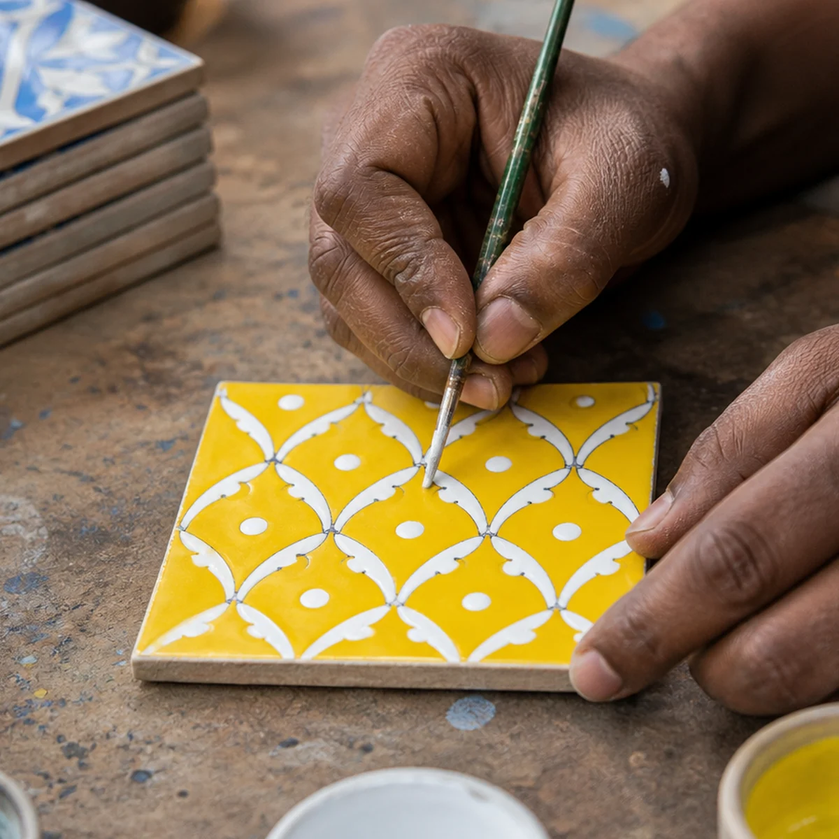 Artisan in Jaipur hand-painting a yellow jaal lattice on a Blue Pottery coaster