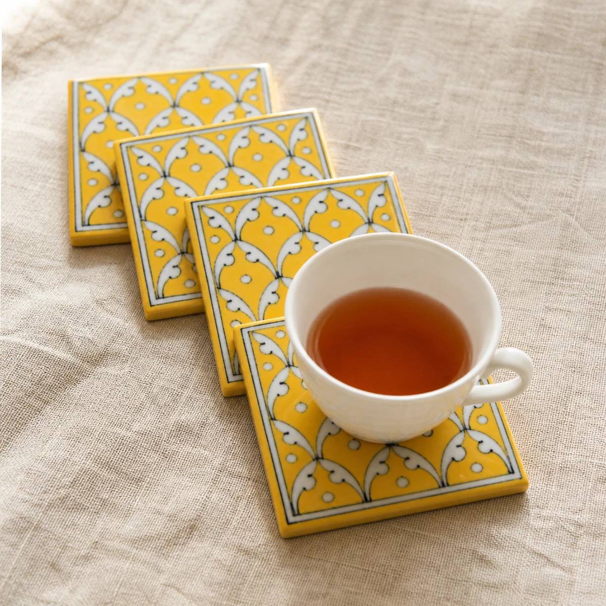 Handmade Jaipur Blue Pottery yellow jaal coaster set of 4 on linen with a tea cup, Rajasthan India