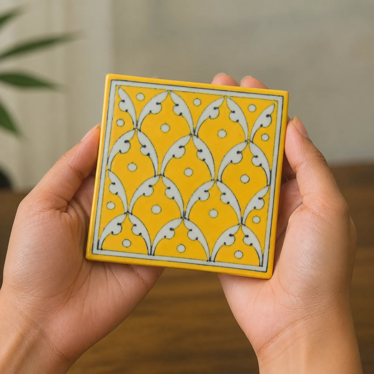 Hands holding a 4-inch square Jaipur Blue Pottery yellow jaal coaster to show scale