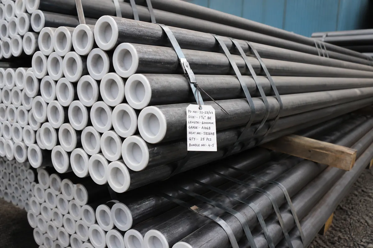 Close-up of nested ERW steel pipe export bundle with end caps, steel strapping, and OD/wall tags under IS 1239 and ASTM A53
