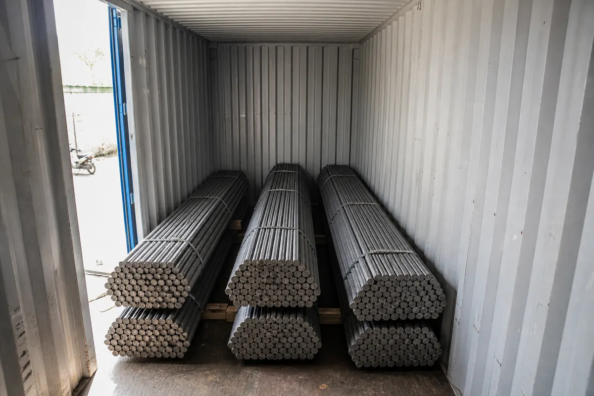 Workers stuffing strapped TMT bar bundles into a 20ft shipping container for FCL steel export from India